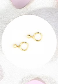 Orecchini a cerchio in oro con un accento sferico, caratterizzati da una finitura lucida e un design circolare, esposti su una superficie rotonda bianca.