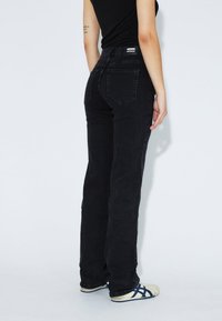 Schwarze Jeans im geraden Schnitt mit hoher Taille, zwei Gesäßtaschen und einem kleinen Markenaufnäher am Bund.