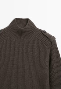 Maglione a coste marrone scuro con alto collo, bottoni sulle spalle e tessuto testurizzato. Il design sottolinea calore e struttura.