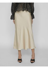 Satinbeige glidkjol med en flödande design, i kombination med en genomskinlig svart topp med blommiga uttagningar och scallopade ärmar. Svarta klackmules.