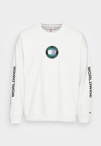 Felpa bianca con maniche lunghe, con un logo rotondo che presenta un globo e la scritta "TOMMY JEANS SINCE 1985." Testo "WORLDWIDE" sulle maniche.