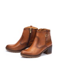 Botines de cuero marrón que presentan una cremallera lateral, un upper texturizado y un tacón bloque mediano. El interior está forrado con un material más claro.