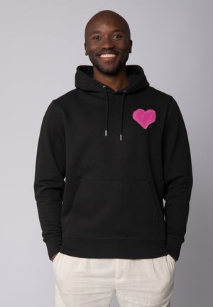 Zwarte hoodie van katoen, met een roze hartontwerp op de linkerborst. Het heeft een kangoeroezak en een verstelbare trekkoordkap.
