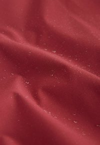 Vodoodporna rdeča tkanina z gladko teksturo, na površini so majhne kapljice vode, ki poudarjajo njene vodoodbojne lastnosti.