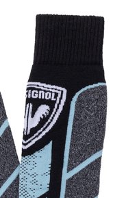 Sorte, grå og blå strikkede skistrømper med forstærkede hæl- og tåsektioner samt et hvidt logo-patch nær kanten.