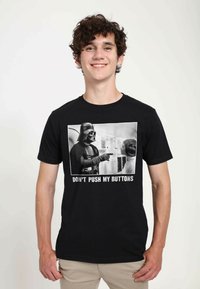 Černé bavlněné tričko s odvážným grafickým potiskem dvou postav na scéně, s bílým textem "NEMEŤ SE MNOU" pod ním.