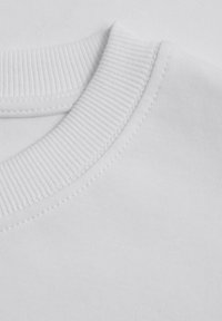 Biała bawełniana koszulka z okrągłym dekoltem, gładka w dotyku, z widocznymi szwami wzdłuż dekoltu.