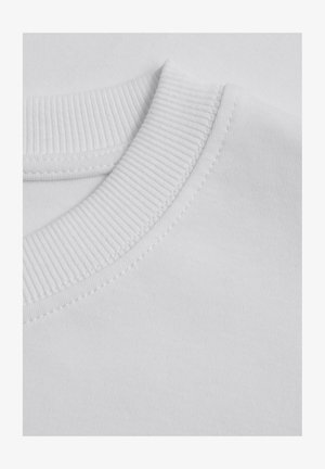 Biała bawełniana koszulka z okrągłym dekoltem, gładka w dotyku, z widocznymi szwami wzdłuż dekoltu.