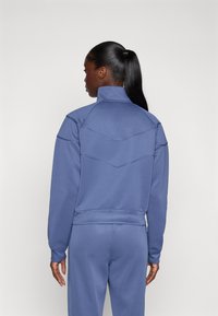 Sudadera azul con cuello alto, rayas texturizadas a lo largo de los hombros y un diseño ajustado. Material suave con un color uniforme.