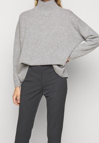 Pull gris en maille avec col roulé, poignets côtelés et fentes latérales, associé à un pantalon tailleur gris foncé. Texture douce, coupe décontractée.