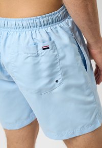 Lichtblauwe zwemshorts met een elastische tailleband, zijzakken en een achterzak met een klein logo in rood, wit en blauw.