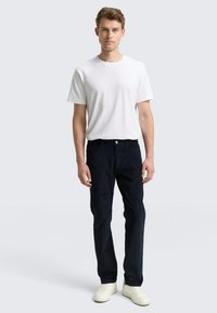 Biała koszulka z okrągłym dekoltem, ciemnoniebieskie jeansy z kieszeniami oraz białe trampki. Jeansy mają klasyczny krój i subtelną fakturę.