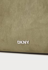 Alyvuogių žalios suede medžiagos krepšys su glotnia tekstūra ir sidabro "DKNY" logotipu. Turi stačiakampio formą ir minimalistinį dizainą.