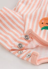 Närbild av rosa och vitt randig babyklädsel med metallknäppen och ett broderat orange ansiktsdetalj.
