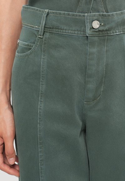 Zelene jeans hlače s prilegajočim dizajnom, vidnimi šivi in sprednjim žepom z zapiranjem na kovinsko gumb.