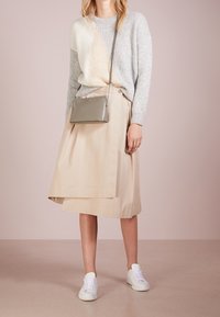 Maglione lavorato a maglia grigio chiaro e crema con dettagli a coste, abbinato a una gonna avvolgente crema e sneakers bianche. Include una piccola borsa a tracolla grigia.