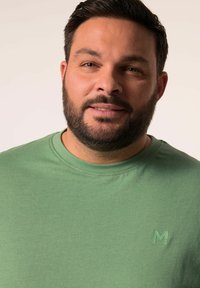 Zelené bavlněné tričko s kulatým výstřihem a jemným logem značky v odpovídající zelené barvě na hrudi. Měkká textilie s volným střihem.