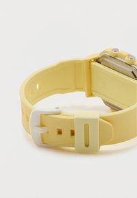 Κίτρινο ρολόι χειρός με λευκό πόρπη και ορθογώνιο κάσα, εμφανιζόμενο από πίσω σε λευκό φόντο.