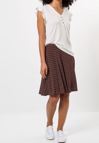 Haut blanc à col en V avec manches courtes à volants et détail à trois boutons, associé à une jupe marron longueur genou avec motif géométrique.