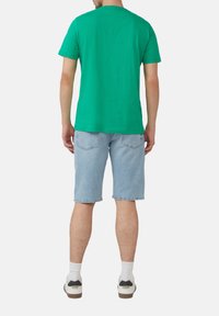 Groen t-shirt met korte mouwen, gemaakt van katoen, relaxte pasvorm, gedragen met lichtblauwe denim shorts, achteraanzicht, witte enkelsokken en sneakers.