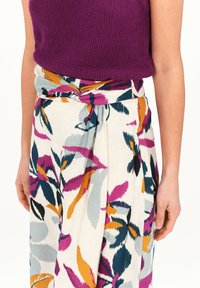 Top sin mangas de punto morado combinado con una falda envolvente multicolor con estampado floral que presenta patrones de hojas en rosa, naranja y azul. Tejido texturizado.