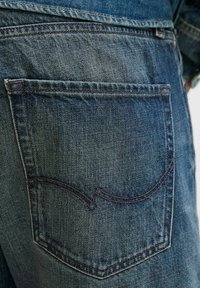 Jeans din denim de culoare albastru închis au o singură buză pe spate cu detalii de cusătură arcuată. Materialul are o finisare texturată cu estompare subtilă.