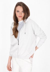 Grijze zip-up hoodie van zacht materiaal, met een trekkoordcapuchon, geribbelde manchetten en een relaxte fit. Draag het over een gestreept shirt.