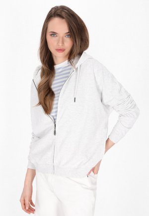 Grijze zip-up hoodie van zacht materiaal, met een trekkoordcapuchon, geribbelde manchetten en een relaxte fit. Draag het over een gestreept shirt.