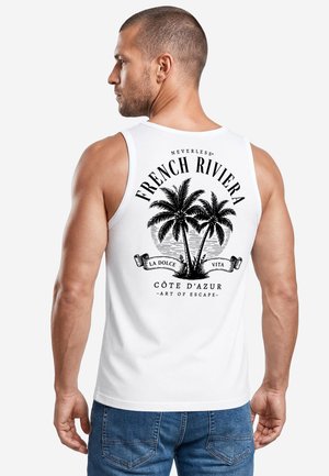 Mann, der nach links schaut, trägt ein weißes ärmelloses Shirt mit schwarzem Palmenmotiv und dem Text "French Riviera, La Dolce Vita, Côte d'Azur" auf dem Rücken.