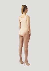 Nackter Bodysuit mit Rundhalsausschnitt und nahtlosem Design; kombiniert mit beige farbenen High Heels. Glatte Textur und figurbetonter Schnitt.