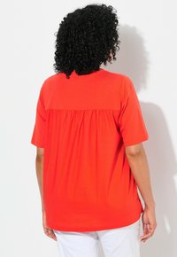 Top rosso a maniche corte con design a schiena arricciata, realizzato in tessuto morbido, caratterizzato da una vestibilità rilassata e orlo curvo. Nessun motivo o dettaglio particolare.