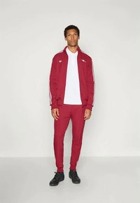 Bordo trenirka z belimi črtami; jopica z zadrgo in oprijete hlače; teksturirano blago; ujemajoča se bela majica; črne športne čevlje.