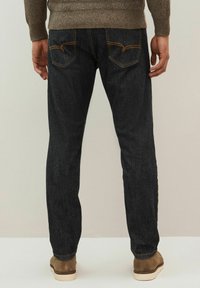 Jeans negre din denim cu un croi drept, cusături portocalii, două buzunare pe spate, purtate cu o pereche de pantofi din suede maro și un pulover tricotat.