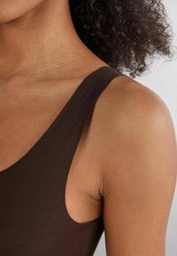 Top marrón sin mangas con escote redondeado, que cuenta con un material suave y elástico y un diseño ajustado, enfatizando los hombros y la parte superior del brazo.