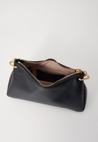 Black leather handbag with a gold zip closure, open to reveal a beige lining and a small interior pocket. Features a curved shape and gold hardware.