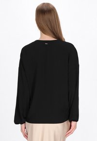 Blusa nera con maniche lunghe, scollo rotondo e sottile texture. Presenta un piccolo tag metallico sul retro e un design dalla vestibilità comoda.