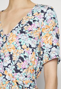 Vestido floral com fundo azul-marinho, adornado com flores laranja e roxas. Decote em V e mangas curtas, ajustado na cintura com um laço.