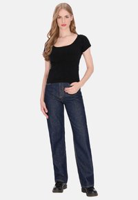 Fekete, rövid ujjú felső mélyen kivágott nyakkivágással, sötétkék, magas derekú, egyenes szárú farmerrel párosítva. A modell fekete cipőt visel.