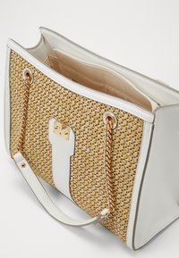 Wykonana z plecionego słomy torebka z dodatkami z białej sztucznej skóry, złotym łańcuszkiem oraz otwarciem na zamek u góry. Wewnątrz znajduje się kieszonka.
