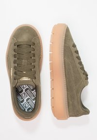 Sneaker in camoscio verde oliva con punta arrotondata, lacci piatti, suola in gomma texturizzata di colore marrone chiaro e soletta con motivo in colori a contrasto.