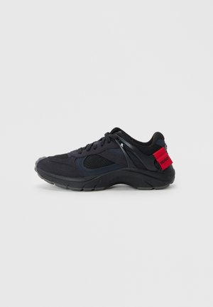 Black athletic shoe featuring mesh and suede materials, rounded toe, cushioned sole, and a red label with "HUGO" on the heel.
