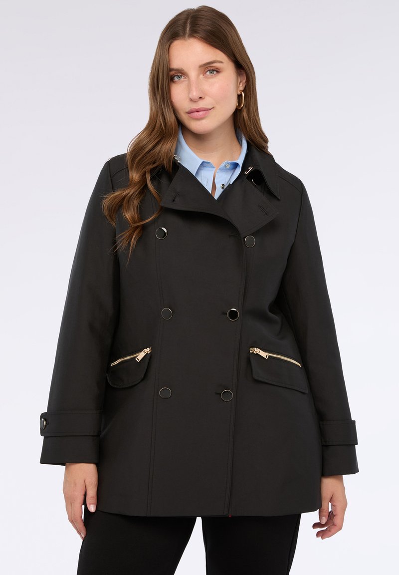 Cappotto doppiopetto nero realizzato in tessuto idrorepellente, con tasche con zip dorate, un colletto ampio e dettagli sui polsini.