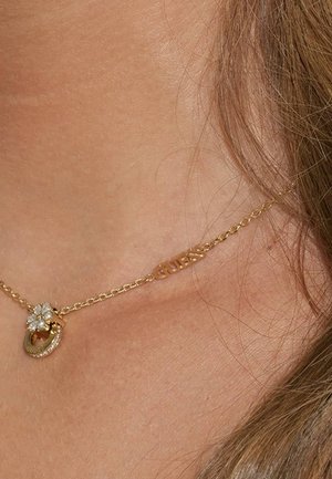 Collier chaîne en or avec un pendentif floral orné de cristaux clairs et un pendentif gravé "GUESS", présentant un design délicat.