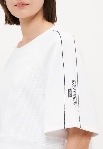 Vit oversize sweatshirt i texturerat tyg. Har svarta detaljer och en logogaffel på ärmen. Korta, vida ärmar.
