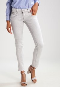 Jeans skinny gris clair en denim doux, dotés de poches avant et d'un design épuré, associés à des sandales à talons hauts beiges.