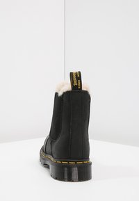 Zwarte leren Chelsea-boot met een voering van bont, elastische zijkanten en een trekflap. Heeft een geel stiksel detail op de zool.
