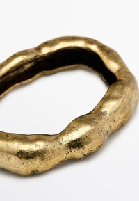 Gouden armband met een onregelmatig, golvend ontwerp, met een gestructureerd oppervlak en een donkere binnenkant met zichtbare slijtageplekken.