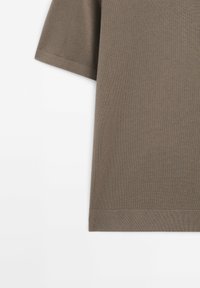 Chemise à manches courtes en tissu tricoté brun avec un design uni, montrée partiellement sur un fond blanc.