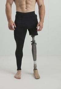 Svarta sportshorts över svarta leggings, med ett metalliskt protesben på höger sida och bar fot på vänster.
