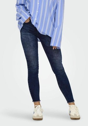 Blauwe en witte gestreepte overhemd met knopen, gecombineerd met donkerblauwe skinny jeans en beige sneakers. De jeans hebben een ruwe zoom en een slim fit ontwerp.